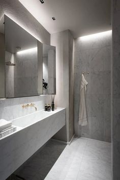 A high-end marble bathroom with a custom white marble sink, gold faucet and a three-panel mirror