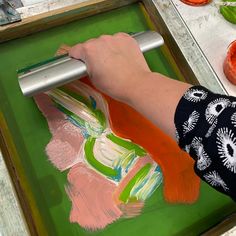 a person is using a roller to paint on a piece of paper with oranges and green