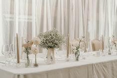 there are many vases and flowers on the table with white linen draped curtains behind them