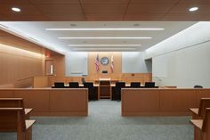 an empty courtroom with chairs and desks on the floor, in front of a large american flag