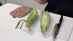 two corn cobs sitting on top of a cutting board with a knife next to it