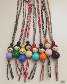 a bunch of different colored beads with faces on them hanging from strings in the shape of people