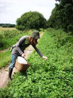 a woman picking weeds in a field with a basket on her shoulder and wearing a hat