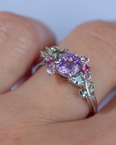 a woman's hand holding a ring with an amethorate and multicolored stones