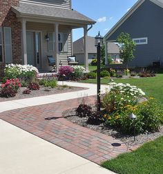 a brick walkway leading to a house with flowers in the front yard and landscaping around it