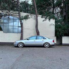 a silver car is parked in front of a building with trees and bushes around it