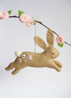 a stuffed rabbit hanging from a branch with flowers on it's head and ears