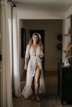 a woman in a white dress holding a wine glass and walking down a hallway way