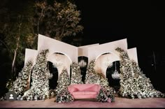 a pink couch sitting in front of a white arch covered in flowers and vines at night