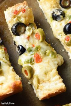 three slices of pizza with olives, peppers and cheese on top sitting on a baking sheet