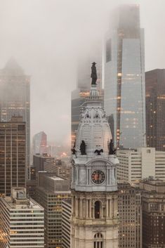 a clock tower in the middle of a city with skyscrapers behind it and foggy skies