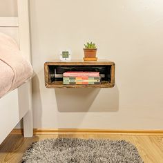 a shelf with books and a plant on it in the corner of a room next to a bed