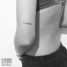 the back of a woman's shoulder with tattoos on it, which reads chaos