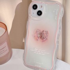 an iphone case with a pink bow on it next to a candle