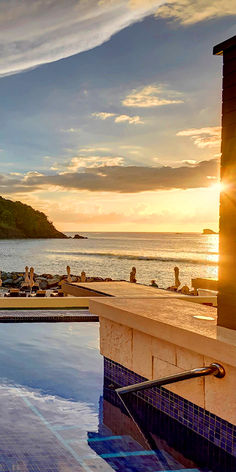 an outdoor swimming pool with the sun setting in the background and people lounging around