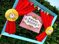 a circus themed photo frame with red curtains and yellow ribbons around it, on top of a green bush