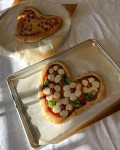 two heart shaped pizzas sitting on top of baking pans next to each other