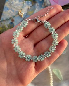 a hand holding a bracelet with green glass beads on it and a white beaded chain