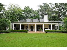 a large white house with columns and pillars in the front yard, surrounded by lush green trees