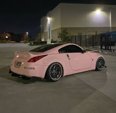 a pink sports car parked in front of a building at night with its lights on