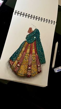 a drawing of a colorful dress on top of a notepad next to a pen