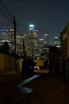 the city skyline is lit up at night, as seen from an alleyway with no traffic