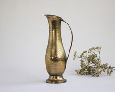 a gold vase sitting on top of a table next to a small flower pot and twig