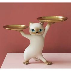 a cat figurine holding two plates on it's back with its paws in the air