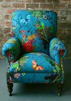 an upholstered blue chair with colorful flowers and butterflies on the armrests