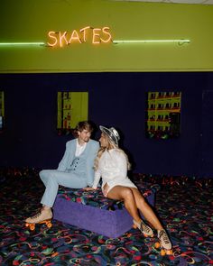 two people sitting on top of a purple bench in a room with neon signs above them