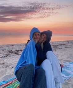 two women are sitting on the beach at sunset