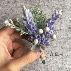 a hand holding a small purple and white boutonniere with flowers on it