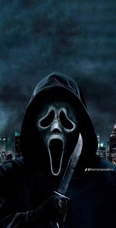 a person in a black hoodie holding a knife and wearing a scary mask with the city lights behind them