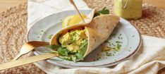 a burrito filled with eggs and greens on a plate next to a jar of mustard