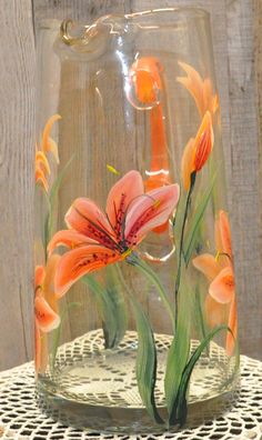 a glass vase with orange flowers painted on the inside is sitting on a doily