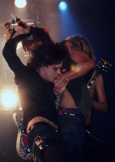 two people on stage with guitars and one person holding his arm up in the air