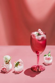 a pink table topped with a wine glass filled with liquid and small pieces of ice