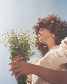 a woman holding flowers in her hands and looking up into the sky with sunshine shining on her face