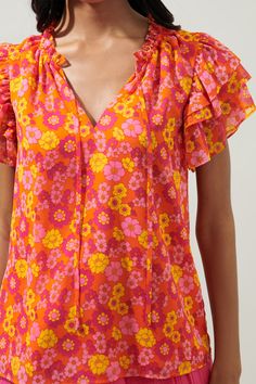 Reminiscent of a vintage print, the Kitt Blouse is a fun and bright way to liven up your wardrobe. Ruffle trim paves the way for the round, split neckline with a tie detail. Ruffle layered sleeves frame a relaxed, chiffon bodice. Wear it tucked into a pair of high rise denim and ballet flats for the ultimate look.- LIghtweight- Split neckline- Relaxed fit- Lined- Color: Orange MagentaSize + Fit - Model is 5'10" and wearing size XS- Measurements taken from size S - Chest: 19 1/2"- Length: 25" Fab Multicolor Butterfly Sleeve Tops With Ruffles, Spring V-neck Blouse With Ruffle Hem, Fitted V-neck Blouse With Vibrant Print, Playful Ruffled Flutter Sleeve Tops, Orange V-neck Blouse With Ruffles, Tie Neck Blouse, Floral Ruffle, High Rise Denim, Chic Boutique