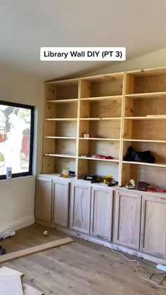 an empty room with wooden cabinets and shelves on the wall, in front of a large window