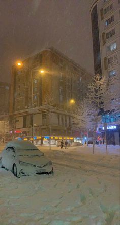 a car covered in snow parked on the side of a street next to tall buildings