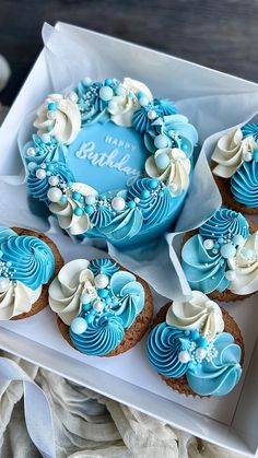 blue and white decorated cupcakes in a box with a happy birthday sign on top