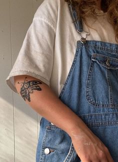 a woman wearing overalls and holding a doughnut in her right hand with a tattoo on the left arm