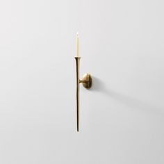 a wall mounted candle holder with a single lit candle on it's side, against a white background