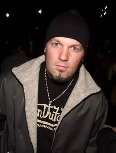 a man wearing a black hat and jacket with a chain around his neck is looking at the camera