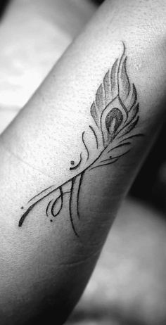 a black and white photo of a woman's arm with a feather tattoo on it