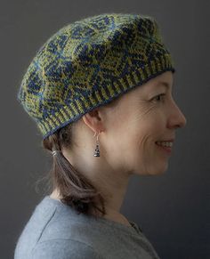 a woman wearing a green and blue knitted hat with silver earrings, looking to the side