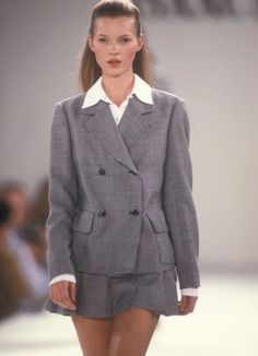 a model walks down the runway in a short skirt and blazer jacket with high heels