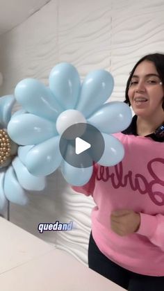 a woman is holding balloons in front of her face and smiling at the camera while standing next to a bed