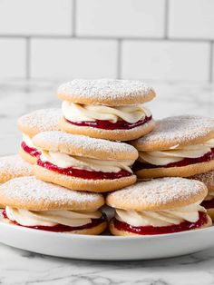 a white plate topped with cookies covered in powdered sugar and strawberry filling on top of a marble counter